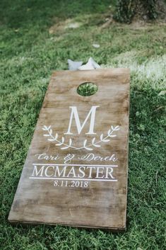 a wooden cornhole board with the initials and date printed on it sitting in grass