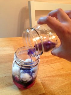 a person is pouring something into a jar on a wooden table with other items in it