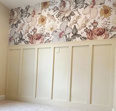 an empty room with white paneling and floral wallpaper