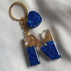 two pieces of blue and gold glittered glass on a keychain, one is shaped like the letter n