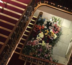 flowers are arranged on the stairs in an old building with red carpet and wooden handrails