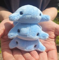 two blue stuffed animals sitting on top of each other in someone's hands,