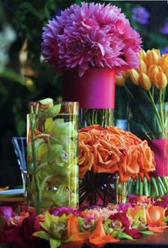 several vases filled with flowers on top of a table next to other glassware