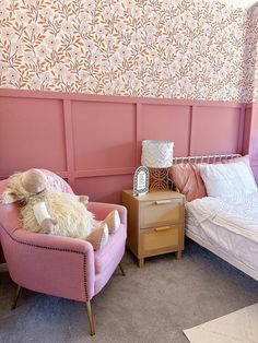 a pink chair sitting next to a bed in a room with wall paper on the walls