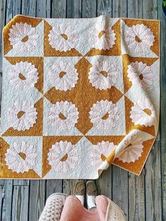 a quilted blanket and pair of slippers sitting on a wooden floor next to it