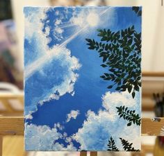 an easel with a painting on it that has clouds and trees painted on it