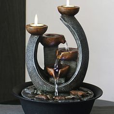 an outdoor fountain with two lit candles in it and water running out of the top