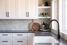 a kitchen with white cabinets and marble counter tops, black faucet, and wooden cutting board