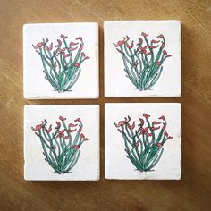 four coasters with red flowers on them sitting on a wooden table, one has green stems and the other is pink