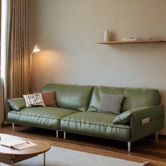 a green leather couch sitting in front of a window next to a wooden coffee table