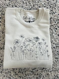 Tot's of love  These beautiful wildflower sweatshirt  Great for birthday Gifts for someone special  Jumper colours  Stone  Black White  Baby pink  Grey  Dusty green  Can be personalised with details under the wildflower design  We can do any colour of thread so if there is a colour you would like please leave when leaving the details for the personalisation Size run  S-34/36in M - 38/40in  L-42/44in Xl-46/48in Xxl-50-52in We have a list of fonts which if you leave the font you would like when. L Cotton Sweater With Graphic Print As Gift, Graphic Print Cotton Sweater As Gift, Graphic Print Cotton Sweater, Custom Embroidery Spring Tops As Gift, Spring Custom Embroidered Top As Gift, Custom Embroidered Tops As Spring Gift, Custom Embroidered Top For Gift In Spring, Spring Cotton Sweatshirt Gift, Spring Crew Neck Sweatshirt