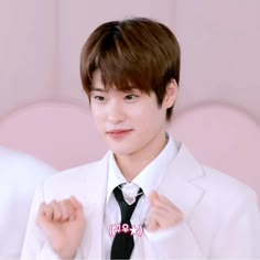 the young man is wearing a white suit and black tie with his hands on his chest