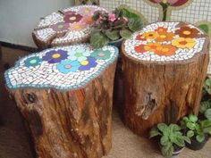 three wooden stumps with mosaic designs on them and flowers in vases next to each other