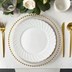 a white plate with gold beading on it next to some silverware and flowers