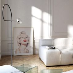 a living room with white furniture and a painting on the wall next to a floor lamp