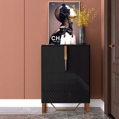 a black cabinet sitting in front of a pink wall with a vase on top of it