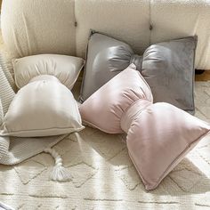 four pillows are arranged on the floor next to a white couch with a gray and pink pillow