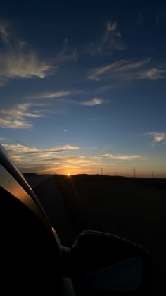 the sun is setting in the distance behind a car's side view mirror on a highway