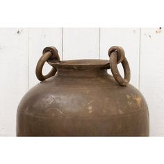 an old brown vase is sitting in front of a white wall with a chain on it