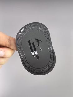 a person holding up a black and silver metal plate with the letter p on it