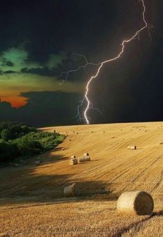 a field with hay bales and lightning in the background