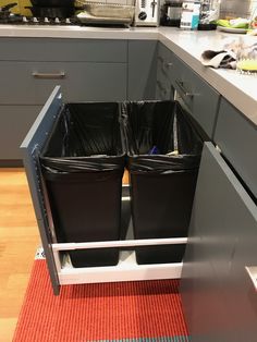 two black trash cans sitting in the middle of a kitchen