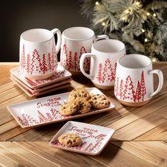 four mugs and three plates with cookies on them sitting next to a christmas tree