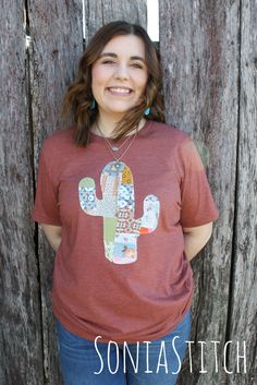 a woman standing next to a wooden fence wearing a red shirt with a cactus on it