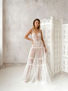 a woman standing in front of a white wall wearing a long dress with sheer fabric