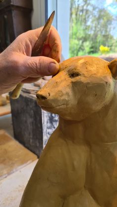 a person is carving a bear out of clay with a pair of scissors in their hand