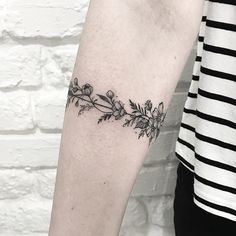 a black and white photo of a woman's arm with flowers on it, in front of a brick wall