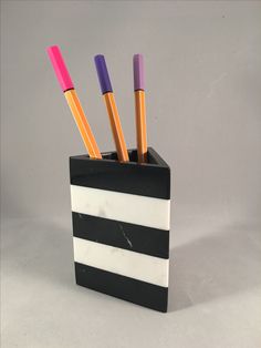 a black and white striped pen holder with four pens in it on a gray background