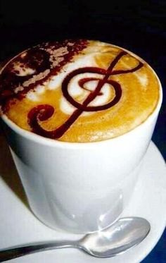 there is a cup of coffee with music on it and spoon next to the cappuccino