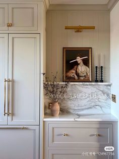 a white kitchen with marble counter tops and cabinets in front of a painting on the wall