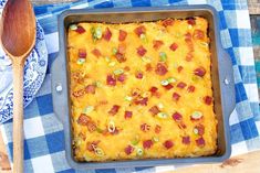 a casserole dish with bacon and green onions on a blue checkered tablecloth