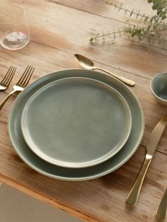 a table set with plates, silverware and gold utensils on top of a wooden table