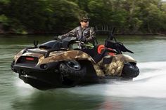 a man riding on the back of a camouflaged watercraft in front of trees