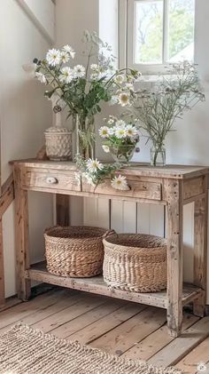 a wooden table with baskets and flowers on it in front of a window next to a stair case