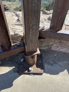 an old metal post with two screws on it and some rocks in the background