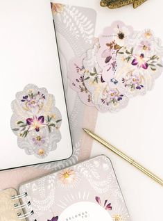 two notebooks with flowers on them next to a pen and flower sticker in the middle