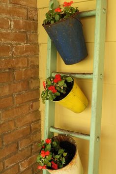 two potted plants sitting on top of a green ladder next to a brick wall