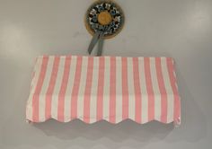 a pink and white striped awning hanging from the side of a wall next to a clock