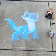 a chalk drawing of a blue dinosaur on the sidewalk next to some crayons