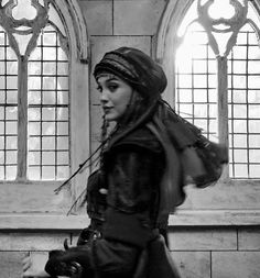 black and white photograph of a woman walking in front of stained glass windows