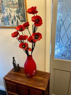 a red vase filled with flowers sitting on top of a wooden table next to a door