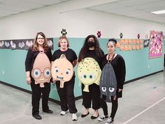 four women are standing in an office with paper cutouts on their faces and body