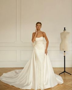 a woman in a white wedding dress standing next to a mannequin on a wooden floor