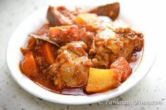 a white plate topped with meat and vegetables covered in gravy on top of a table