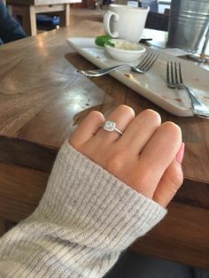 a woman's hand with a ring on it sitting at a table in front of a plate