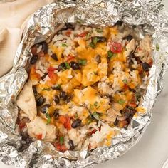 an enchilada covered in chicken, black beans and cheese on top of aluminum foil